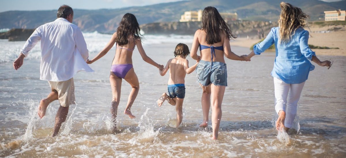 A family having fun running into the ocean on a sunny beach day in Portugal. Joyful and carefree moments.
