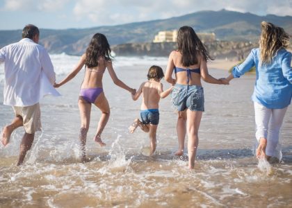A family having fun running into the ocean on a sunny beach day in Portugal. Joyful and carefree moments.