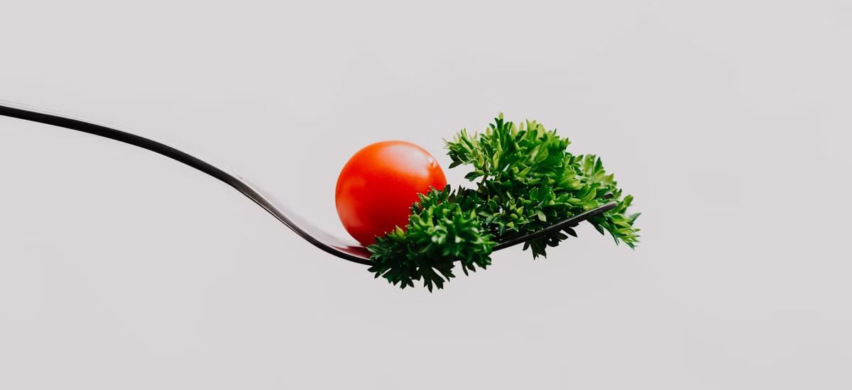 Minimalist close-up of a cherry tomato and parsley on a fork. Perfect for food design.