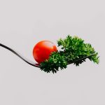 Minimalist close-up of a cherry tomato and parsley on a fork. Perfect for food design.