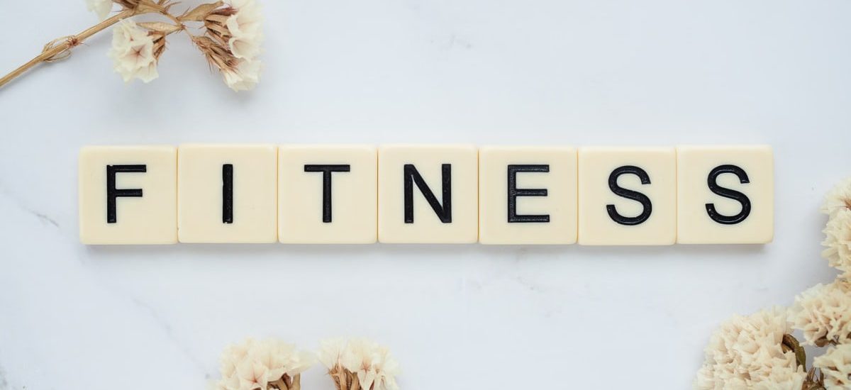 Close-up of scrabble tiles spelling 'FITNESS' on a marble surface with white flowers.