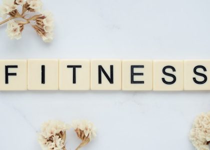 Close-up of scrabble tiles spelling 'FITNESS' on a marble surface with white flowers.